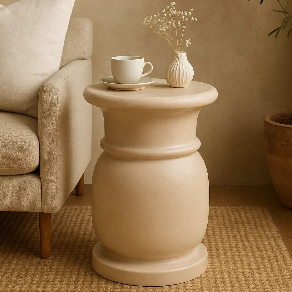 Beige side table with a cup and vase next to a beige armchair in a warm-toned room.