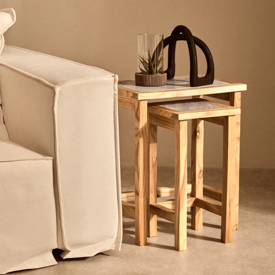 Wooden side table with a plant and decorative item next to a beige armchair against a beige wall.
