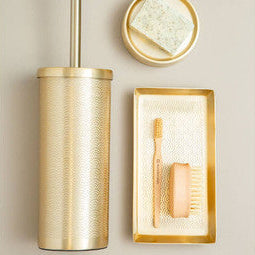 Gold bathroom accessory set including a toilet brush holder, soap dish, and toothbrush holder on a beige wall.