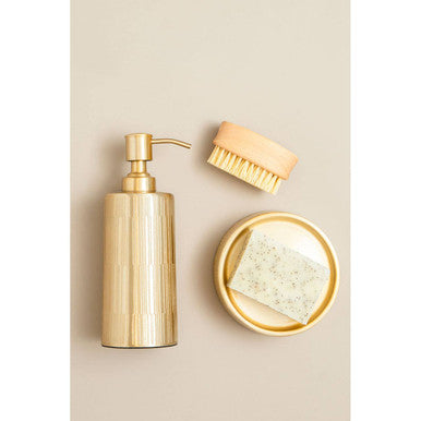 Gold soap dispenser with brush and sponge on a beige background