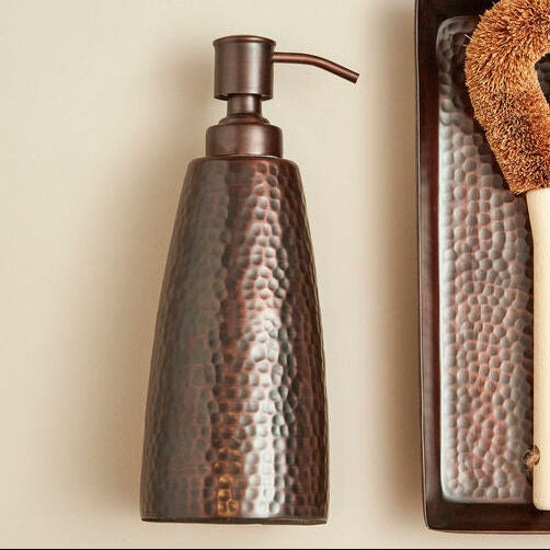 Set of cleaning tools including a soap dispenser, sponge, and scrubber on a neutral background