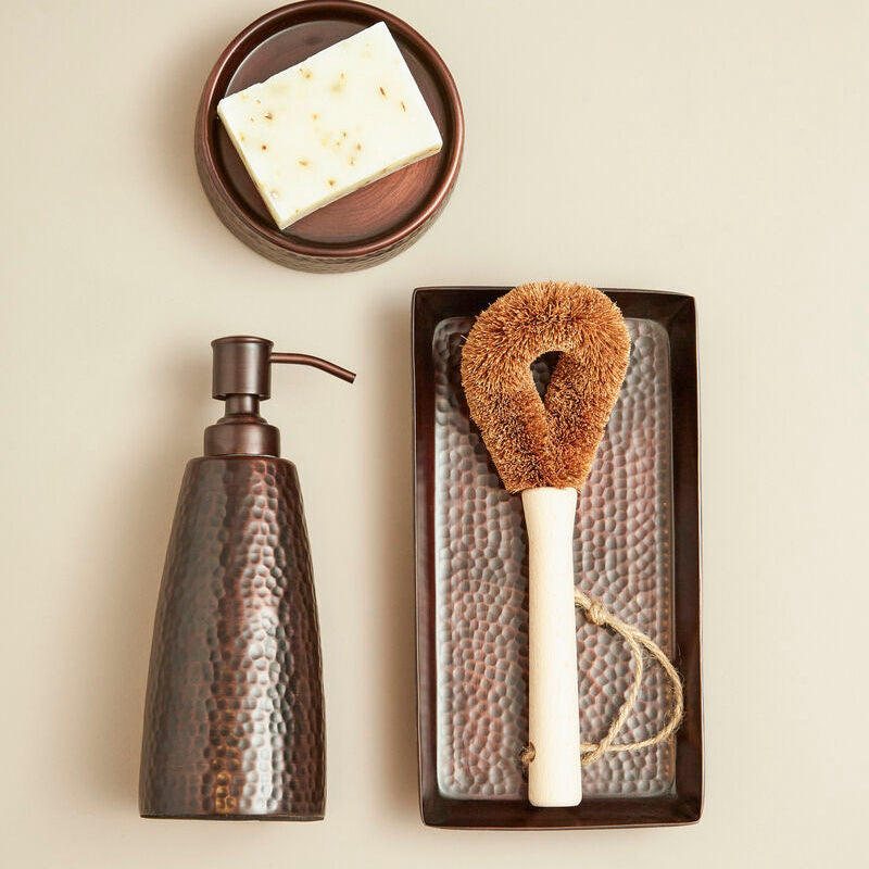 Set of cleaning tools including a soap dispenser, sponge, and scrubber on a neutral background