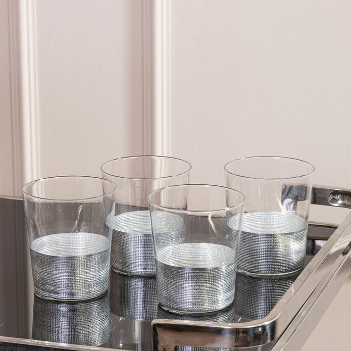 Set of clear glasses with silver bases on a metal tray against a neutral background