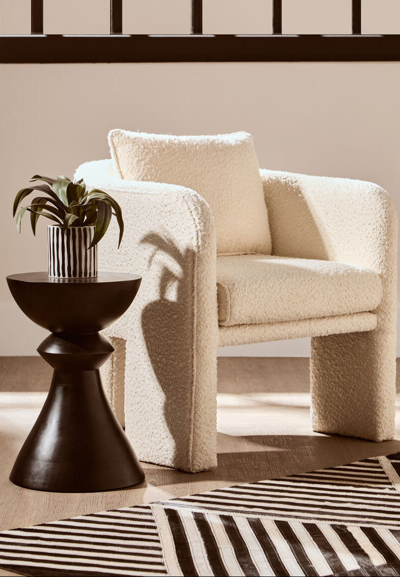 Beige armchair with a plant on a dark wooden side table against a beige wall.