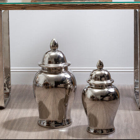 Decorative console table with silver urns, a glass top, and framed artwork on a white wall.