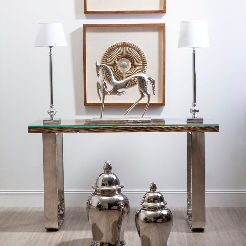 Console table with decorative items including a horse sculpture, lamps, and vases against a white wall.