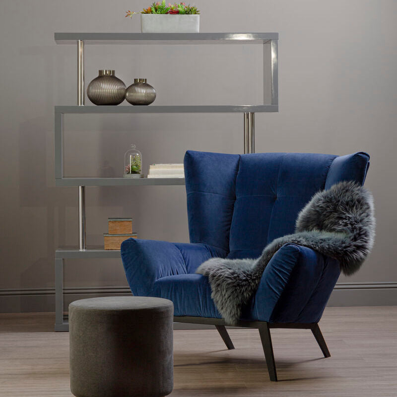 Blue armchair with gray fur throw and gray ottoman in a room with a shelf.