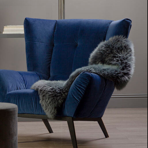Blue armchair with gray fur throw and gray ottoman in a room with a glass shelf.