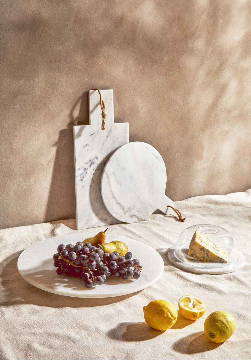 Marble cutting board with fruit and cheese on a neutral background