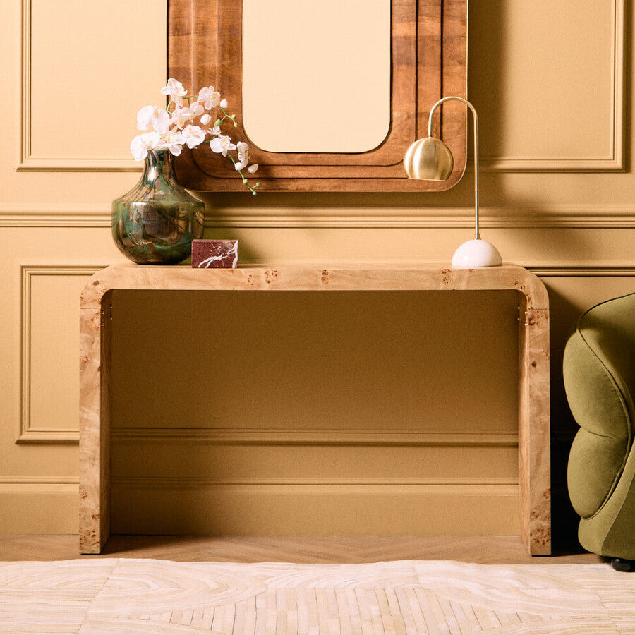 Wooden console table with mirror and decorative items against a beige wall.