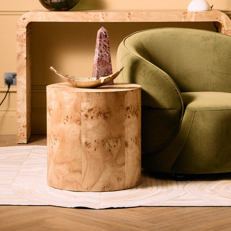 Wooden side table with decorative items next to a green armchair in a room.