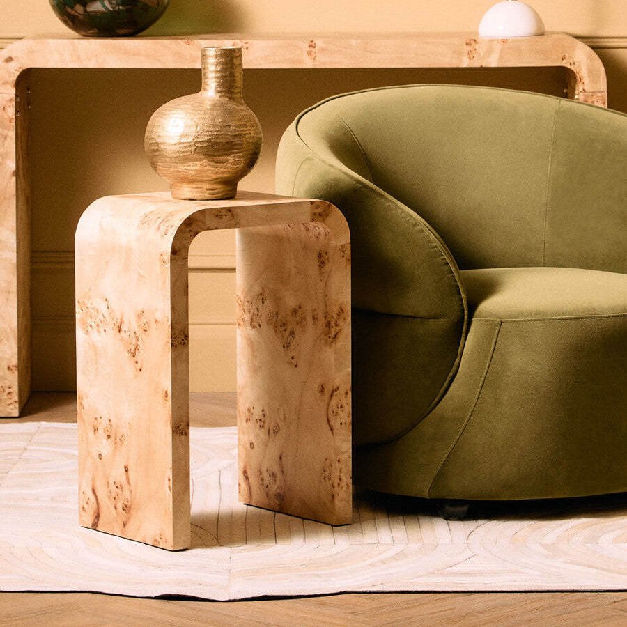 Beige side table with a textured surface next to a green armchair.