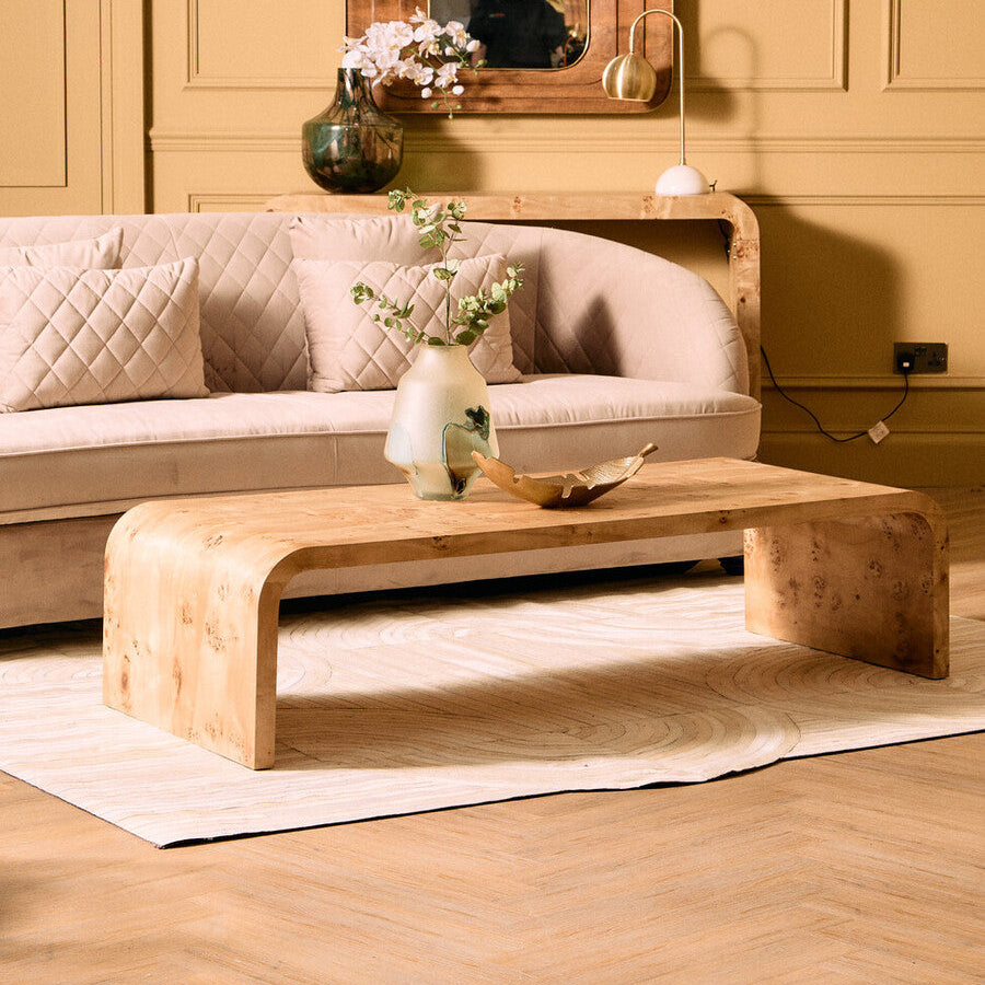 Wooden coffee table in front of a beige sofa with decorative items on a wooden floor.