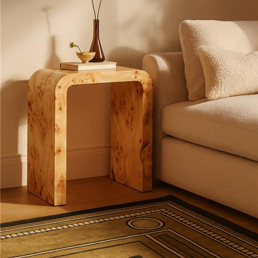 Wooden side table with a vase and books next to a beige sofa in a room with warm lighting.