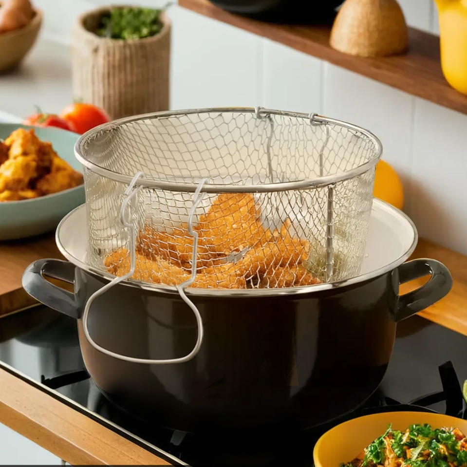Black pot with removable wire basket on a stove, surrounded by kitchen items.