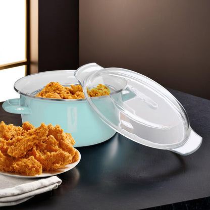 Turquoise ceramic pot with a clear lid on a dark surface, accompanied by fried chicken on a plate.