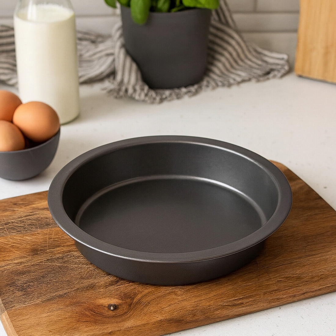 Black baking pan on a wooden cutting board with eggs and a plant in the background
