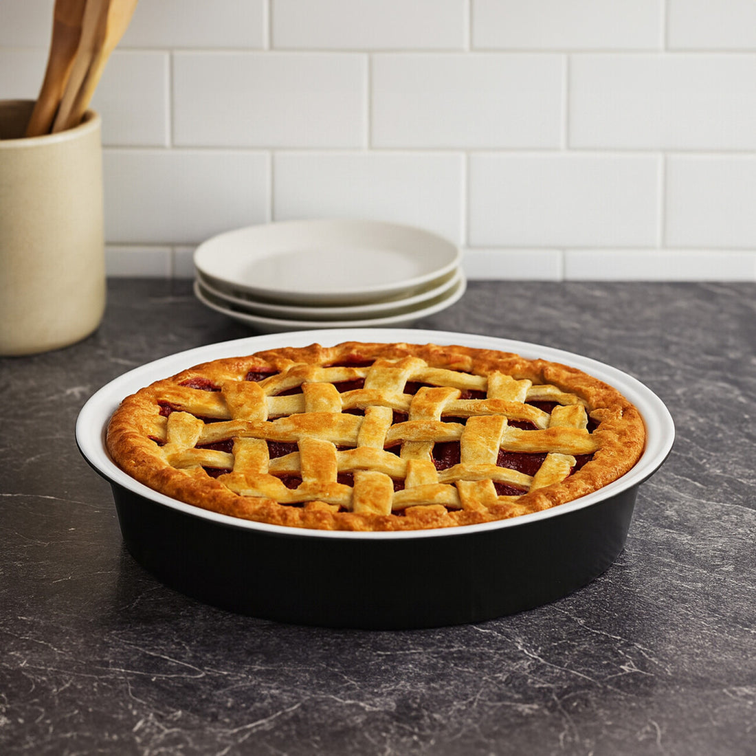 Apple pie in a black pie dish on a dark countertop with white plates stacked in the background.