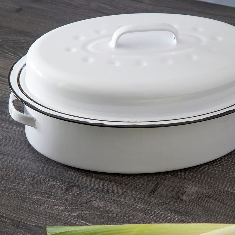 White oval roasting dish with a lid on a wooden surface, accompanied by leeks.