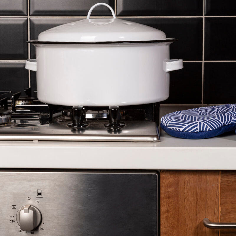 White enameled cast iron Dutch oven on a stove with a tiled wall background