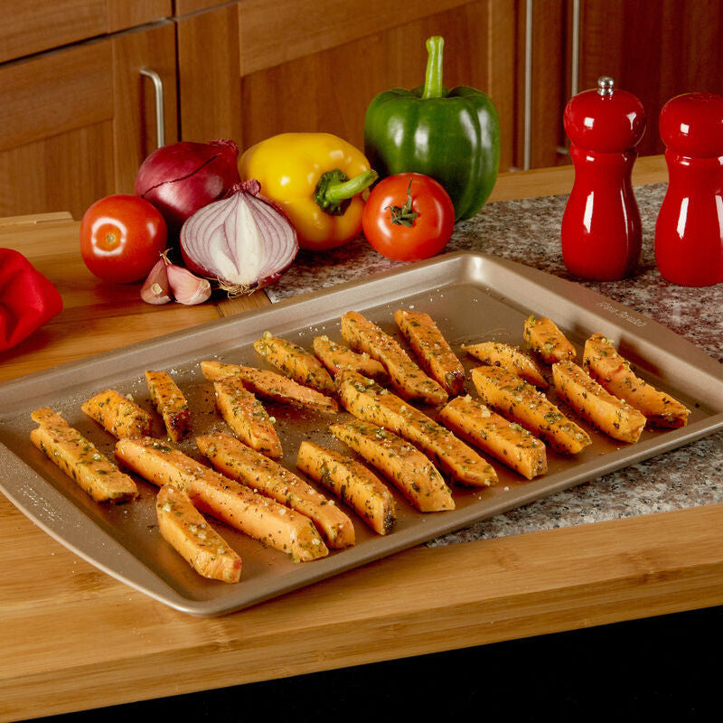 Baked vegetable sticks on a baking tray with vegetables and salt and pepper shakers in the background.