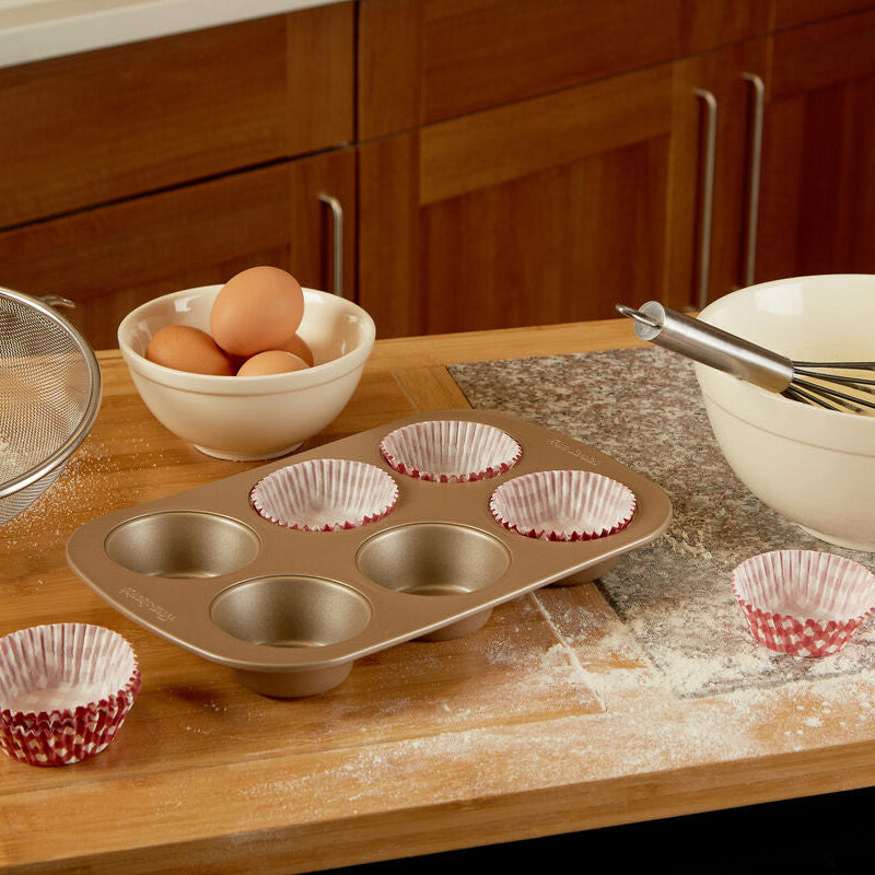 Baking utensils including a muffin tin, mixing bowl, whisk, and eggs on a kitchen counter.