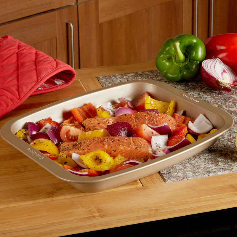 Prepared roasted vegetables on a baking tray with a red oven mitt and lemon on a kitchen counter.