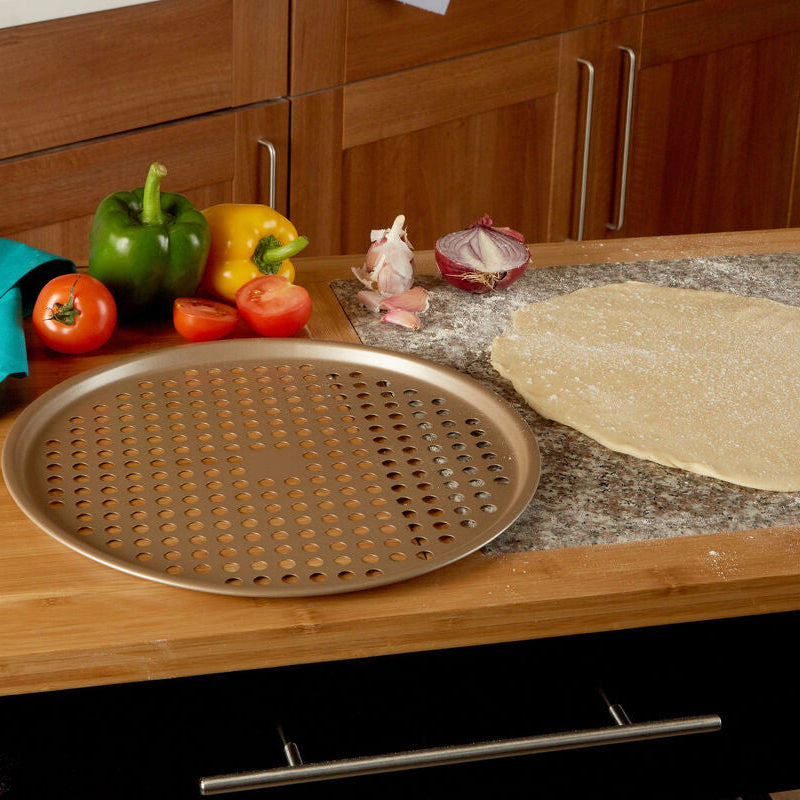 Wooden kitchen counter with pizza dough, vegetables, and a perforated baking tray.