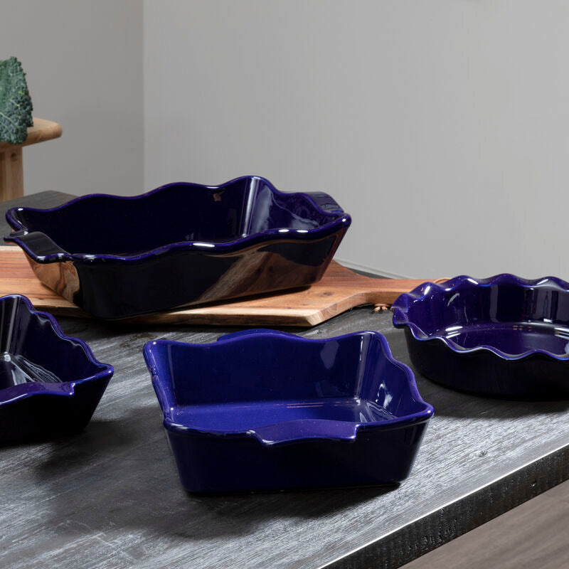 Set of four blue ceramic dishes on a gray surface with green leafy vegetables in the background.