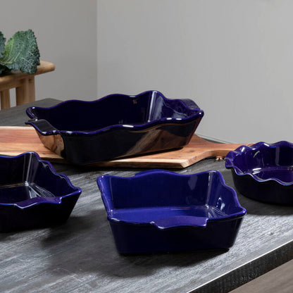 Set of four blue ceramic dishes on a gray surface with green leafy vegetables in the background.