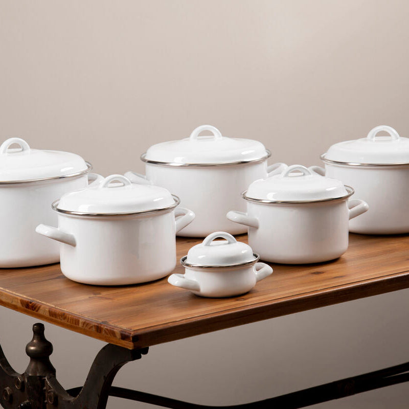Set of white enameled cookware on a wooden table against a beige background