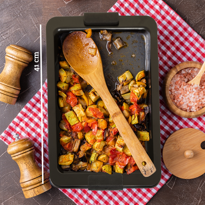 Roasted vegetables in a baking tray with a wooden spoon on a checkered tablecloth.