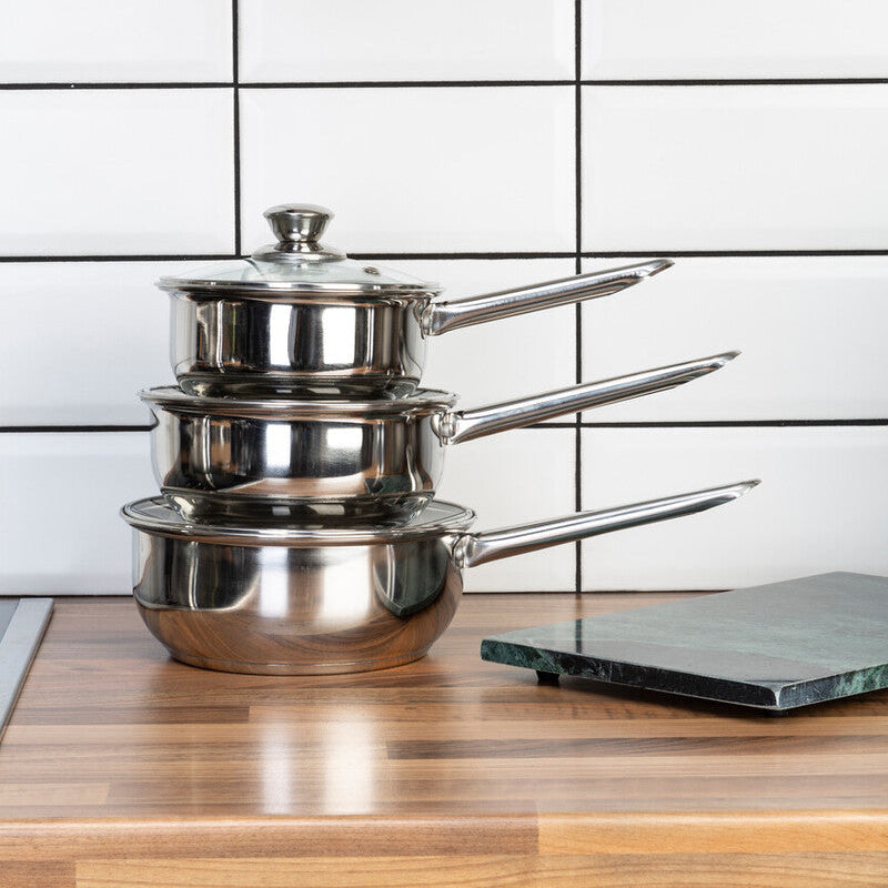 Set of stainless steel cookware on a wooden surface with a tiled wall background