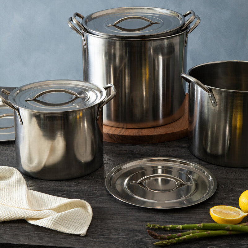 Set of stainless steel pots and lids on a wooden surface with lemons and asparagus.