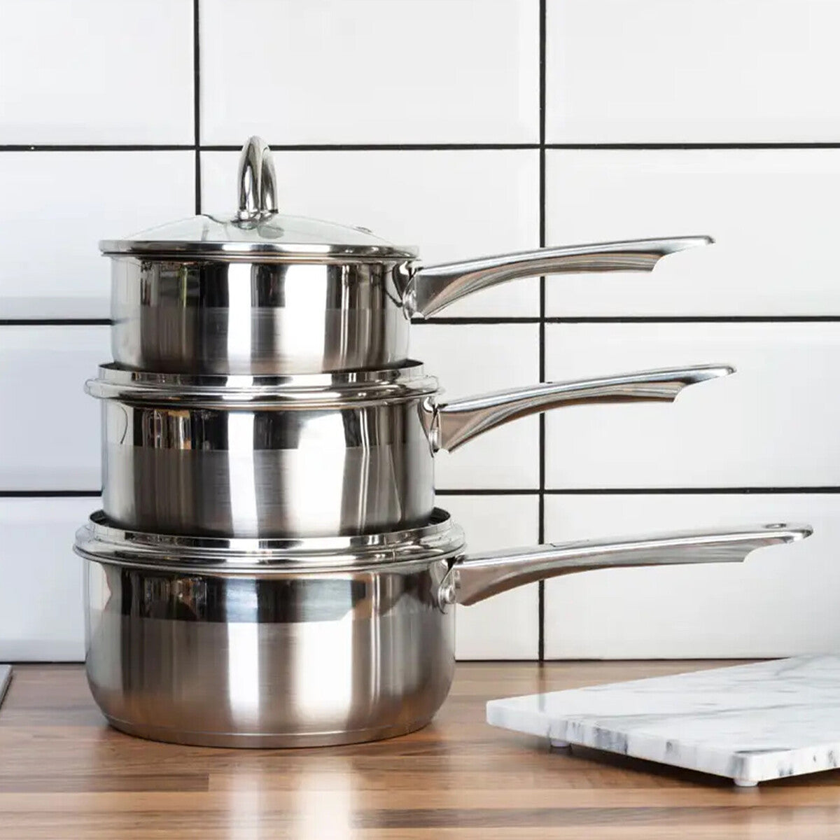 Stack of stainless steel cookware on a kitchen counter with a tiled wall background