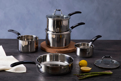Set of stainless steel cookware on a wooden surface with lemons and asparagus.