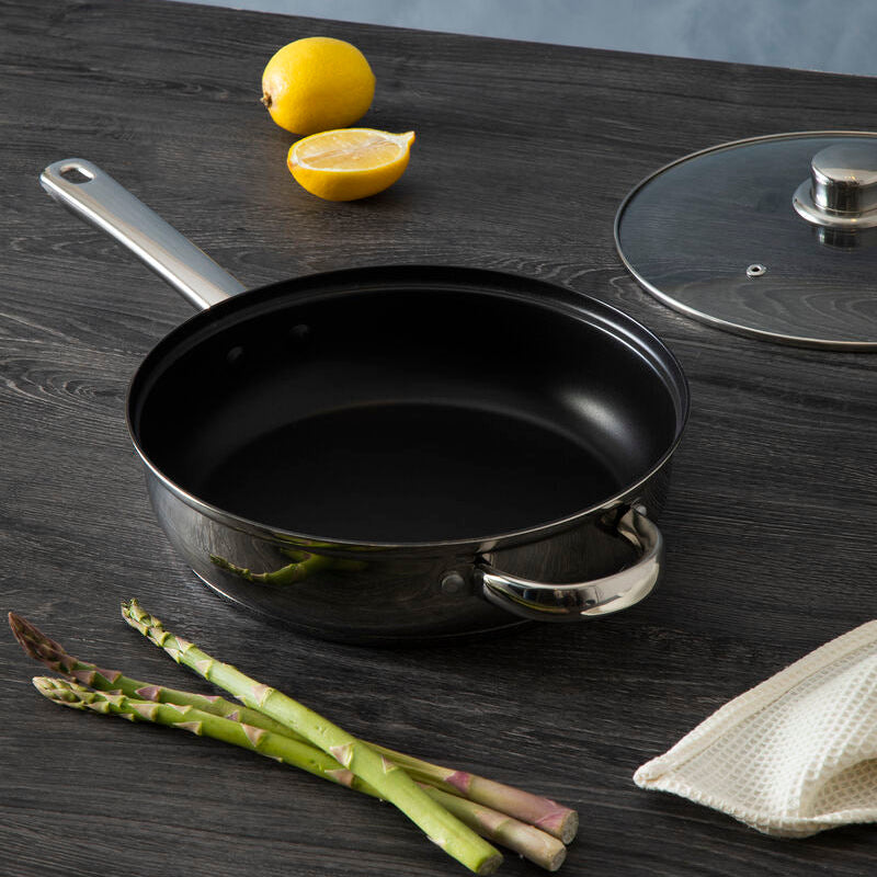 Black frying pan on a wooden surface with lemons, asparagus, and a lid in the background.