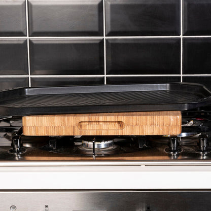 Black griddle on a stove with a wooden handle against a black tiled wall.