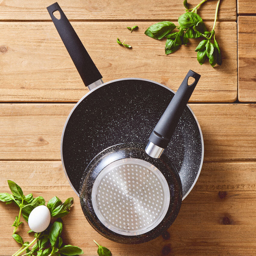 Black frying pan with a white interior on a wooden surface with basil leaves.