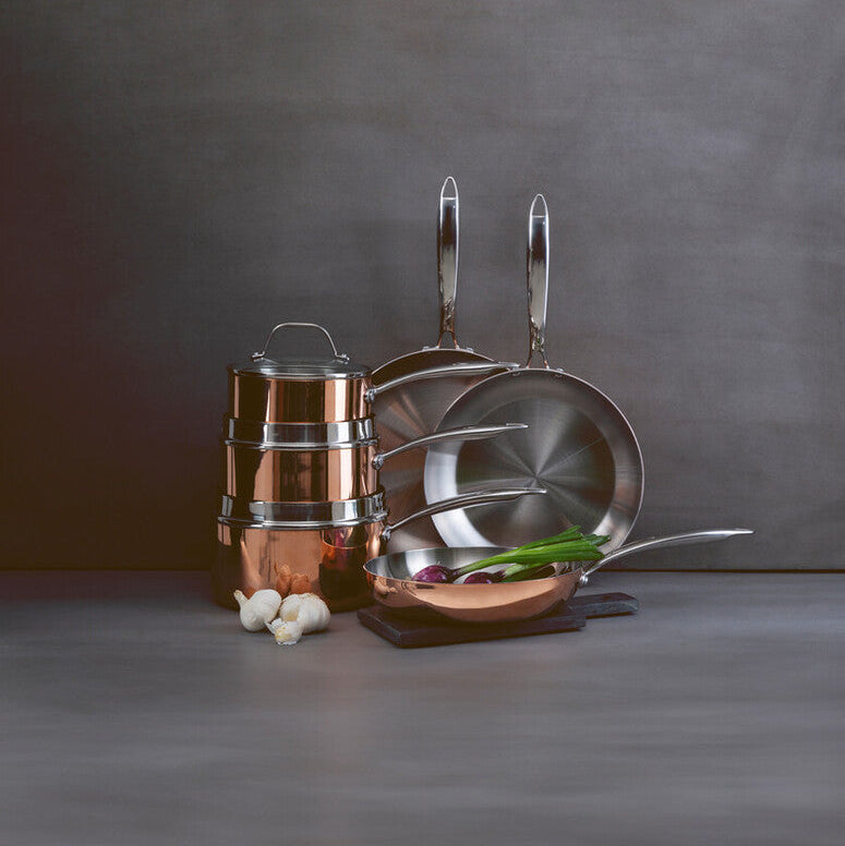 Set of copper cookware including pots, pans, and lids on a gray surface with a dark background.