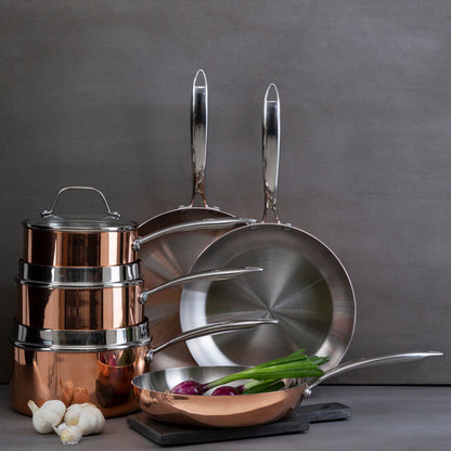 Set of copper cookware including pots, pans, and a strainer on a gray background.