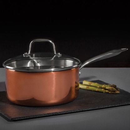 Copper saucepan with lid on a dark surface with asparagus