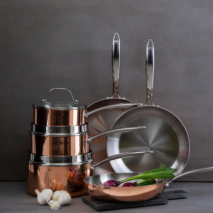 Set of copper cookware including pots, pans, and a strainer on a gray background.