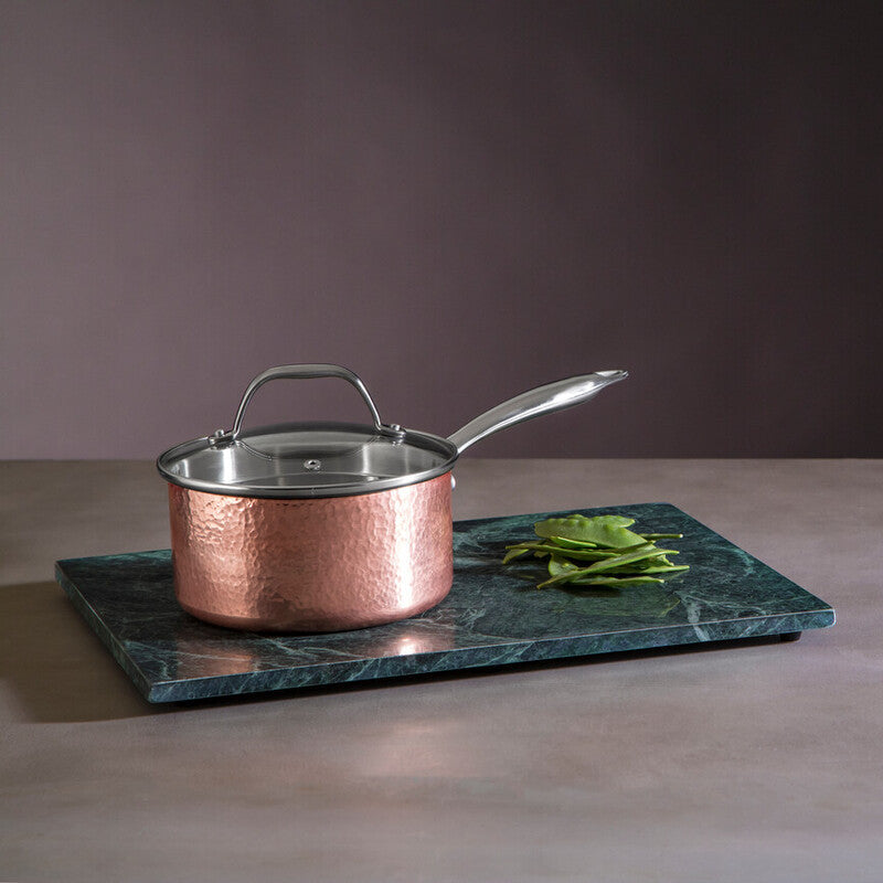 Copper saucepan on a green marble trivet with a dark background
