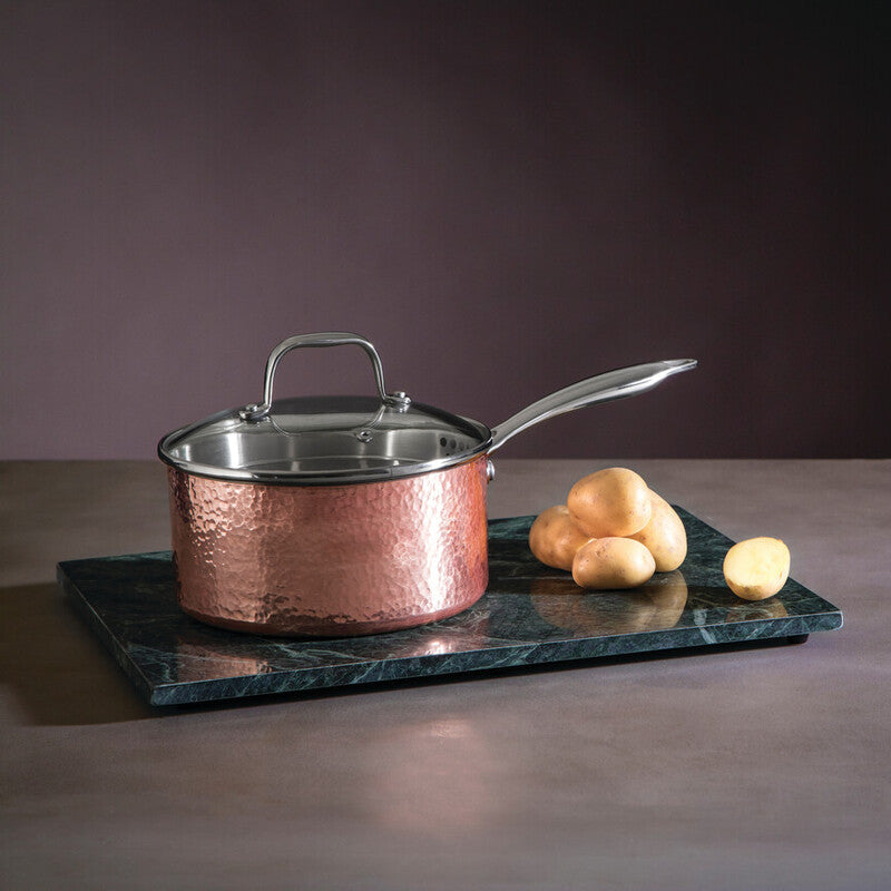 Copper saucepan with lid on a dark marble tray against a dark background