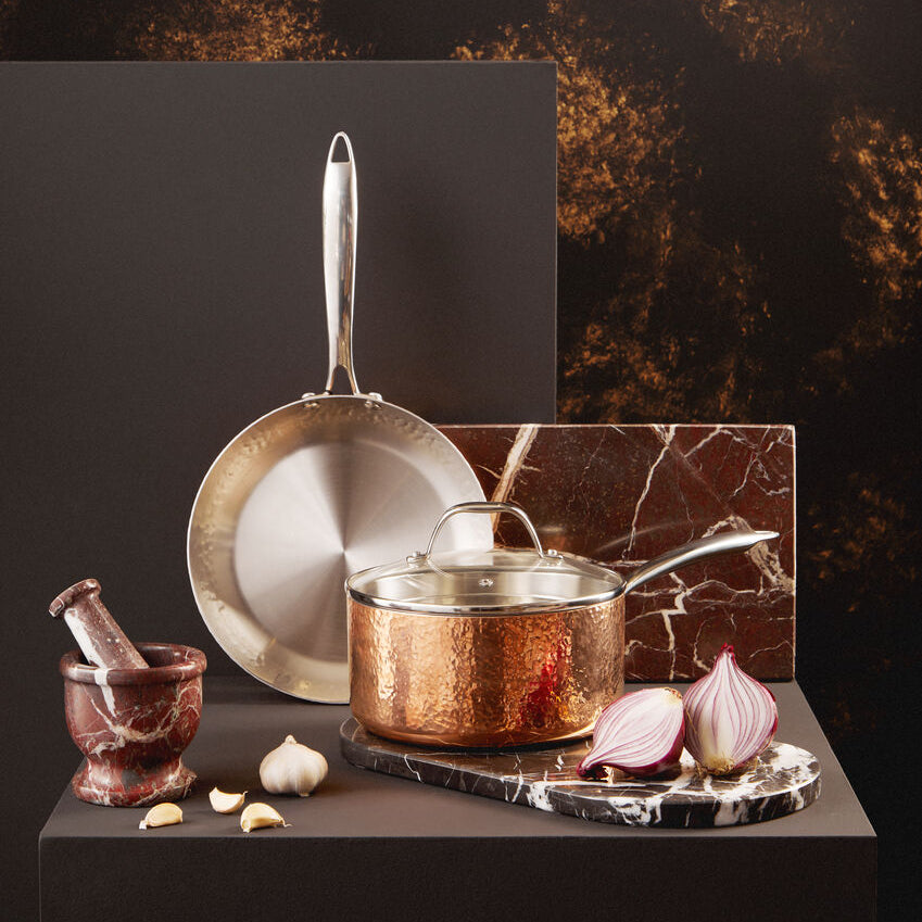 Copper cookware set on a dark surface with a marble pattern