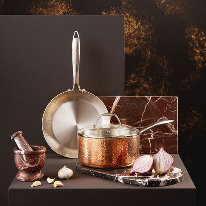 Copper cookware set on a dark surface with a marble cutting board and ingredients.