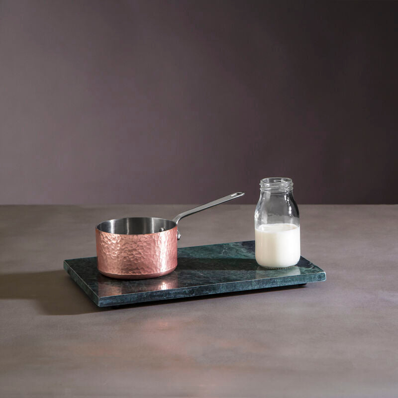 Copper pot and glass bottle on a dark marble tray against a gray background