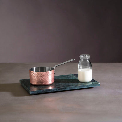 Copper pot and glass bottle on a dark marble tray against a gray background