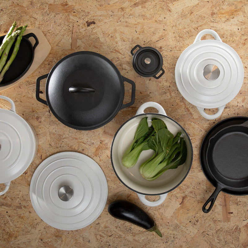 Set of cookware including pots, pans, and bowls on a wooden surface with vegetables.